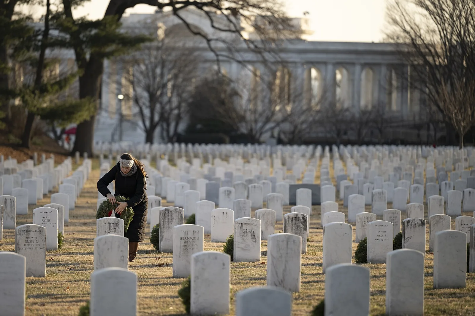 A volunteer lays a wreath at a headstone near the Memorial Amphitheater during Wreaths Across America Day at Arlington National Cemetery.